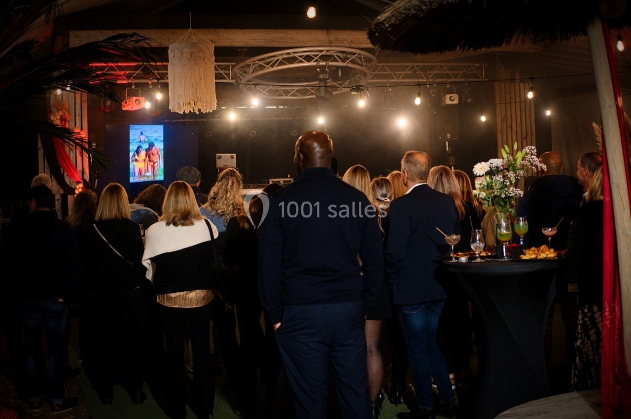 Groupe de personnes debout dans une salle sombre, regardant une scène éclairée avec un écran projetant une image.
