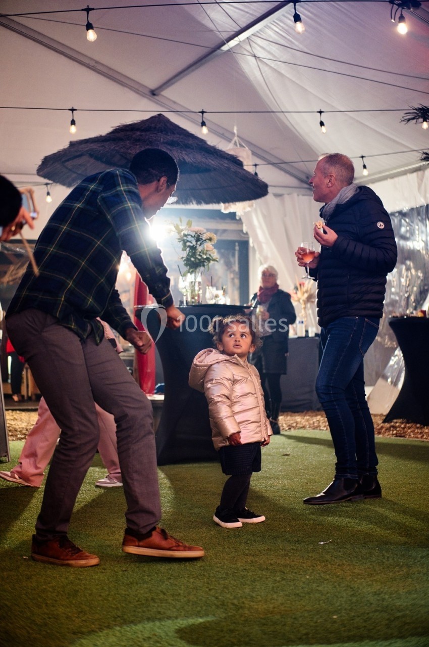 Un homme danse près d'une petite fille regardant autour d'elle sous une tente éclairée lors d'un événement festif.