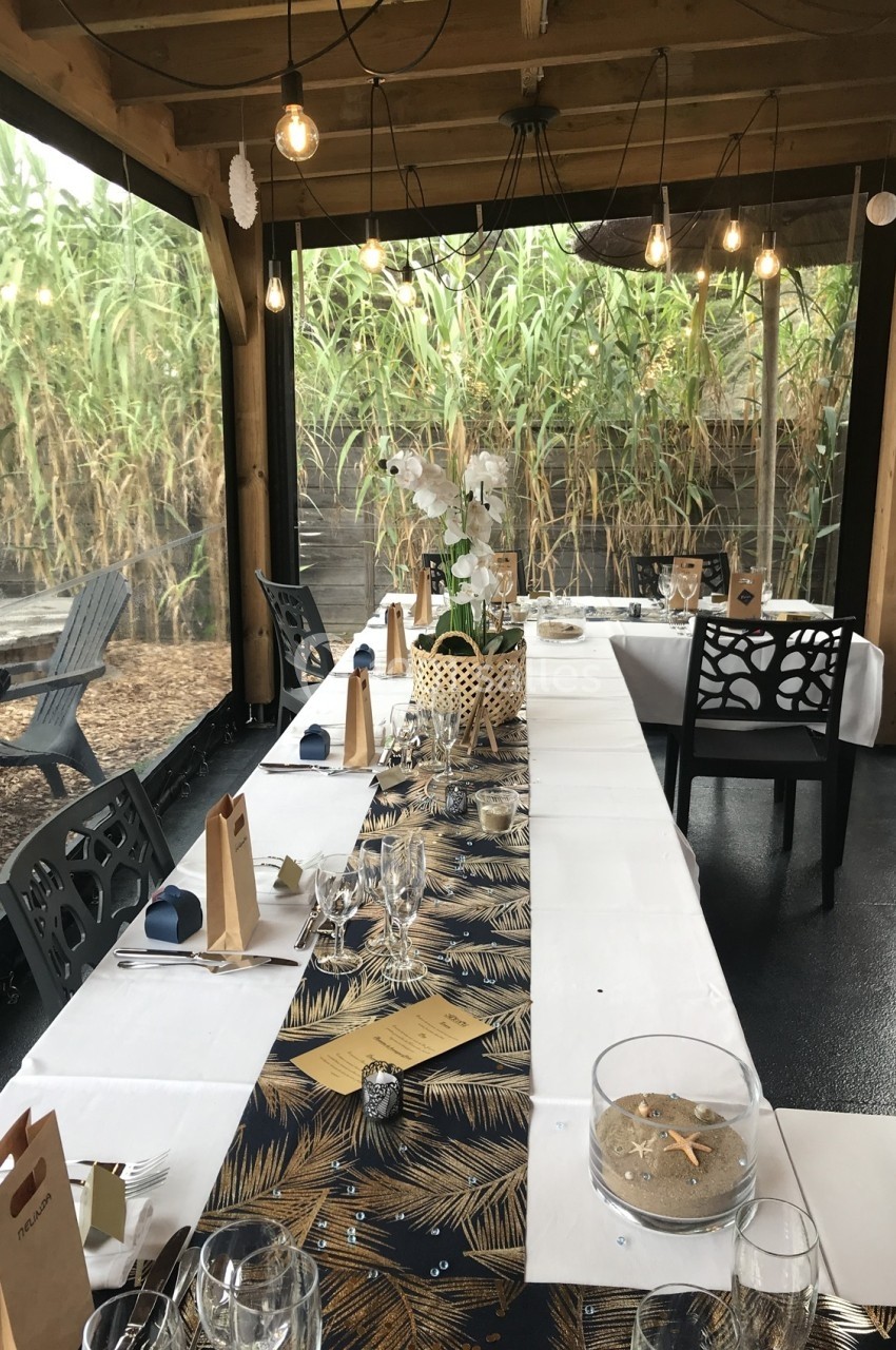 Table décorée pour un repas, avec nappes à motifs, vaisselle élégante et vue sur un jardin bordé de bambous.
