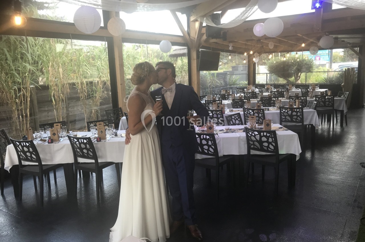 Un couple en tenue de mariage s'embrasse dans une salle de réception décorée avec des tables dressées.