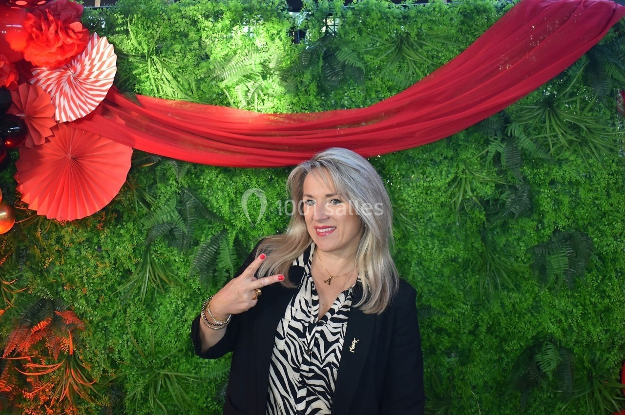 Femme souriante posant devant un mur végétal décoré de draperies rouges et d'éventails.