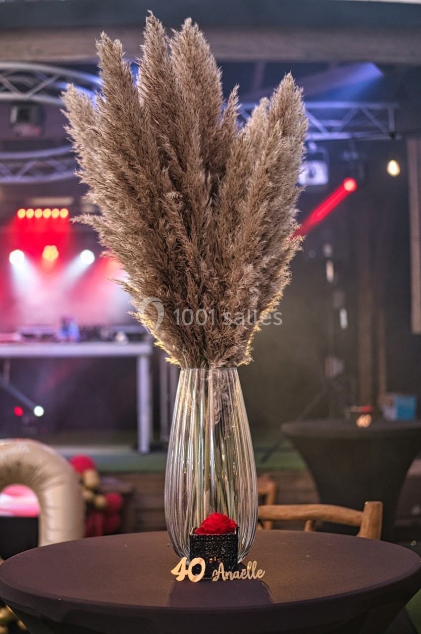 Vase en verre contenant des herbes de la pampa, posé sur une table décorée pour un événement festif.