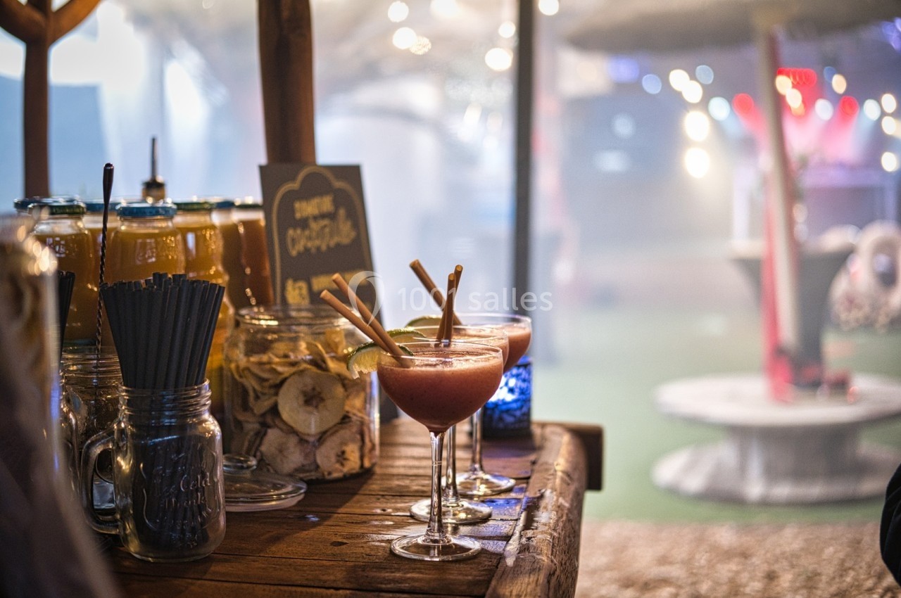 Stand de boissons avec cocktails colorés, bocaux de fruits secs et ambiance lumineuse en arrière-plan.