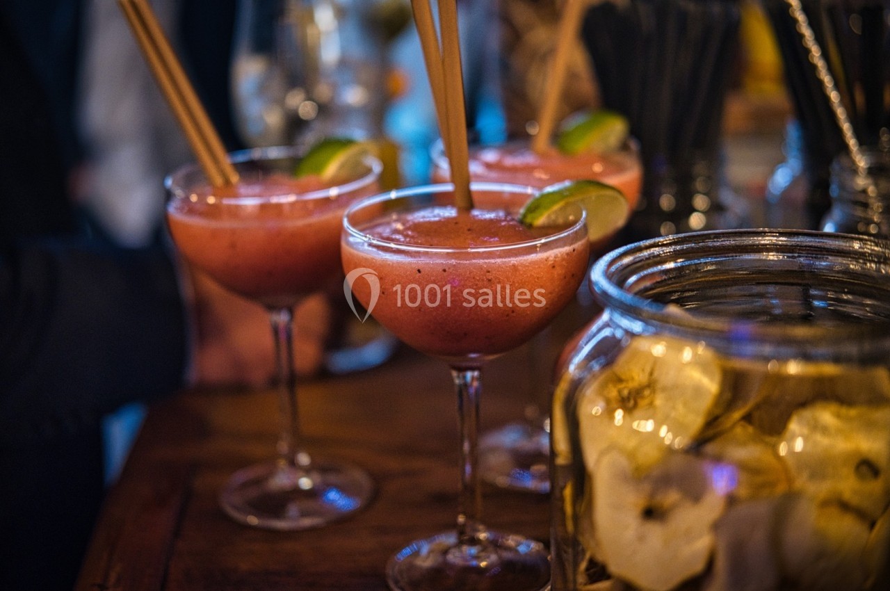Trois cocktails rouges servis dans des verres à pied, garnis de rondelles de citron vert et de pailles en bois.