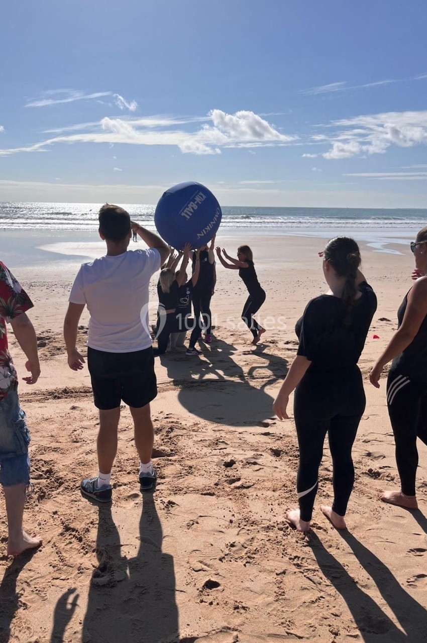Des personnes jouent avec un grand ballon bleu sur une plage ensoleillée, près de l'océan.