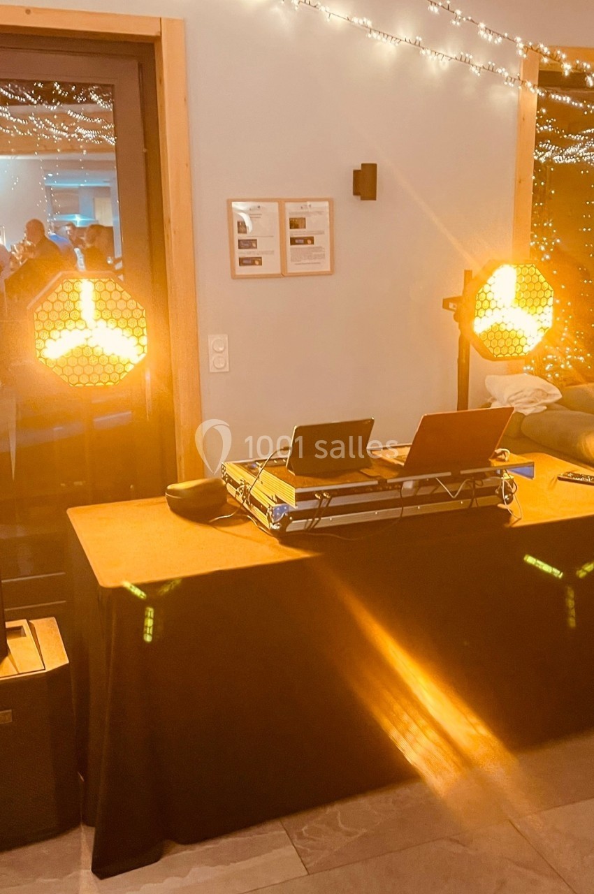 Table de DJ équipée de matériel audio et éclairée par des projecteurs orange dans une salle décorée de guirlandes lumineuses.