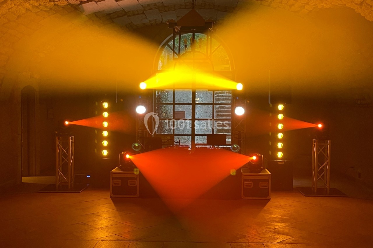 Jeu de lumières colorées illuminant une scène avec équipement audio dans une salle voûtée en pierre.