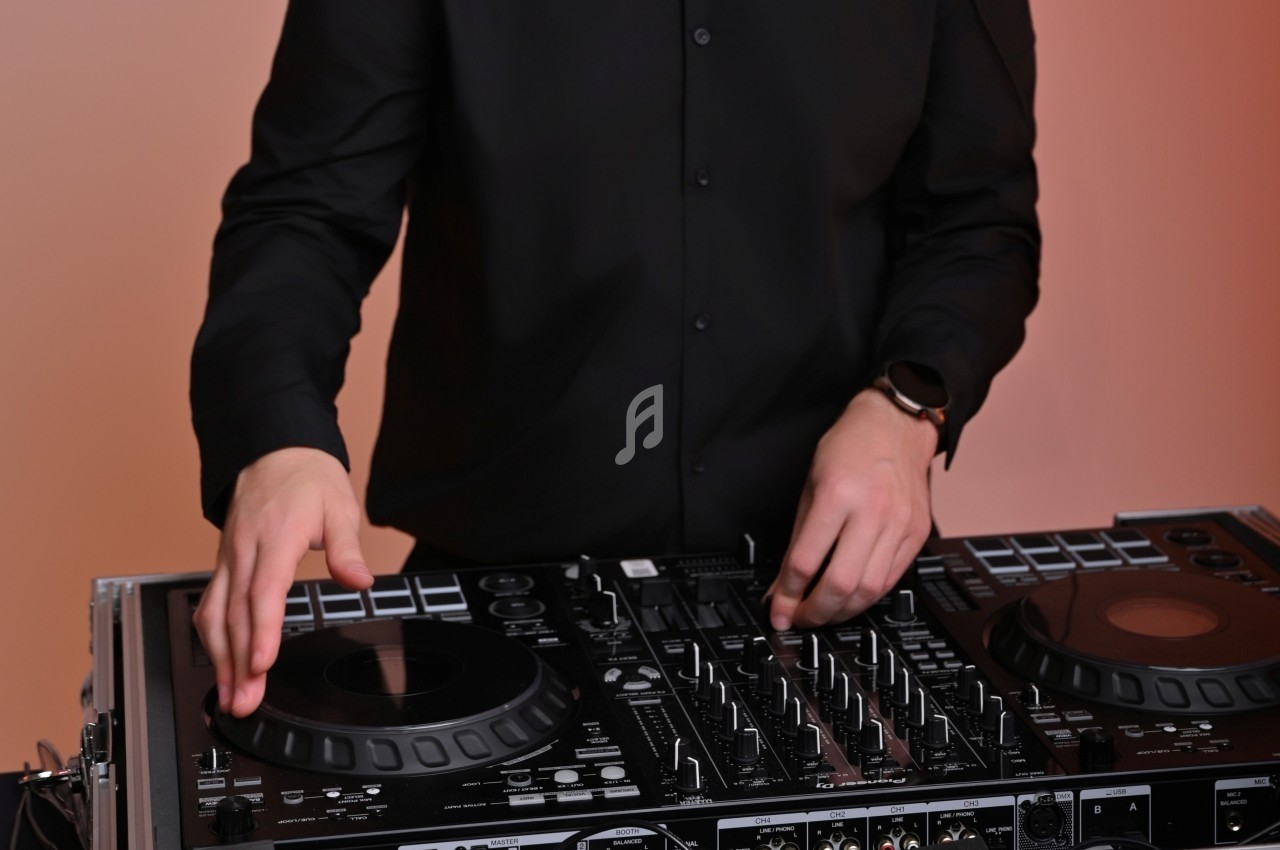 Personne en chemise noire utilisant une table de mixage avec des platines et des commandes audio.