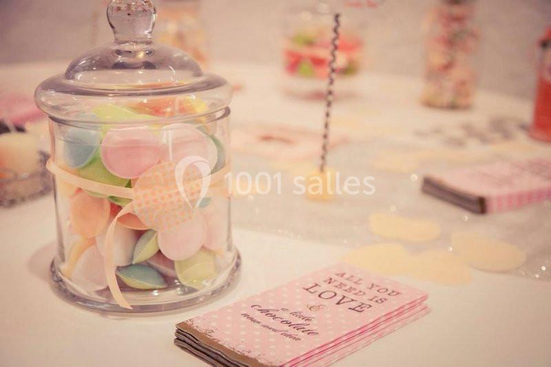 Bocal en verre rempli de bonbons colorés sur une table décorée avec des cartes et des éléments pastel.