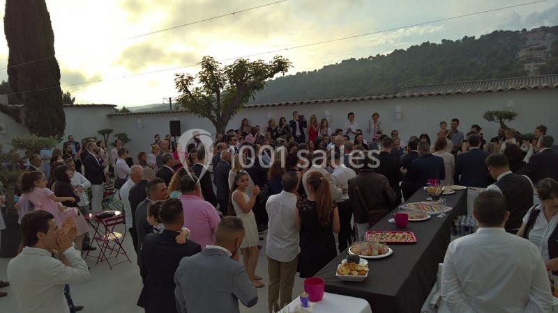 Groupe de personnes réunies en extérieur pour un événement, avec des tables de buffet et un paysage de collines en arrière…