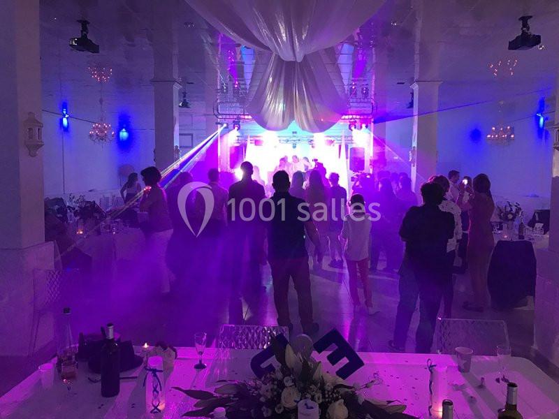 Salle de réception avec des invités dansant sous des lumières colorées et une décoration suspendue au plafond.