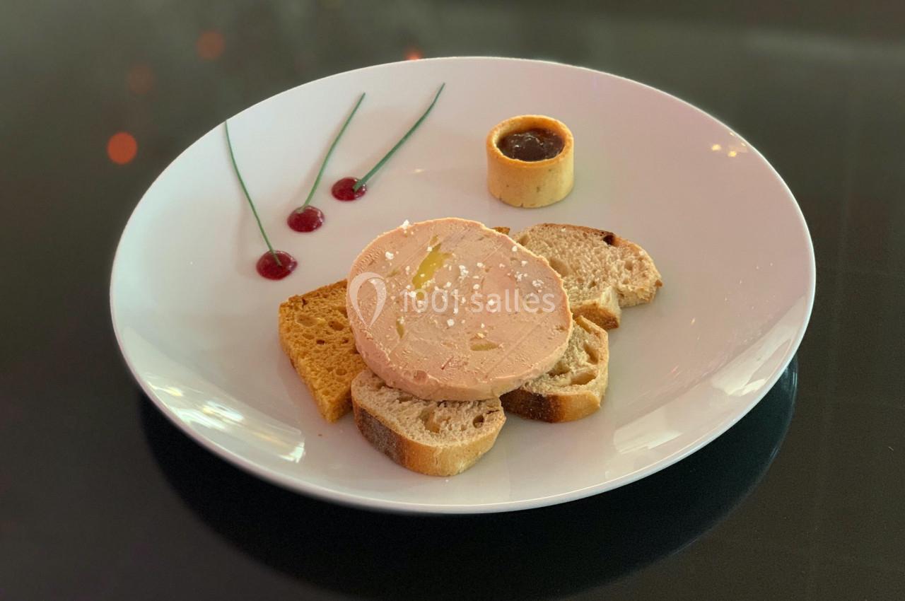 Assiette de foie gras avec tranches de pain, gelée rouge, et accompagnement de confiture dans un décor raffiné.