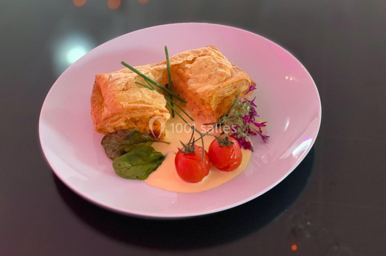 Assiette avec deux feuilletés dorés, accompagnés de tomates cerises, sauce crémeuse et garniture de verdure.