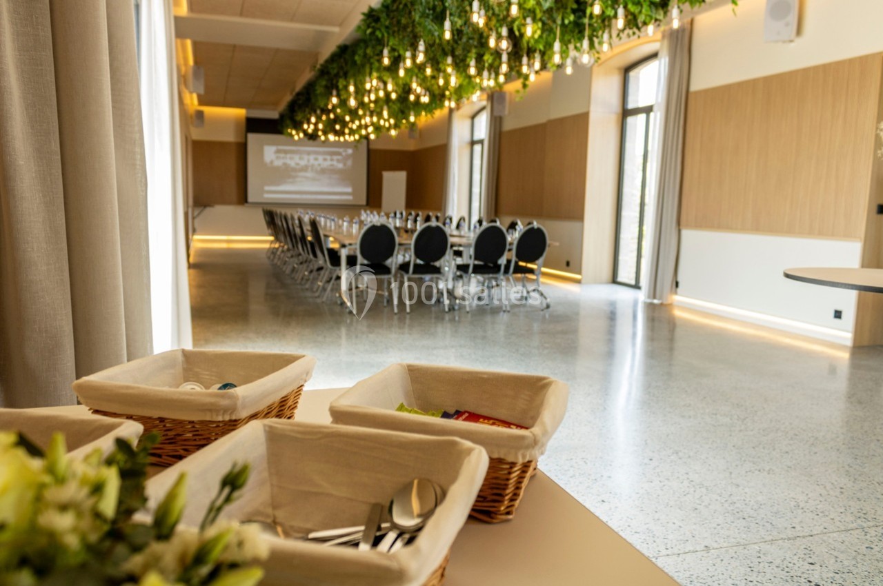 Salle de réunion lumineuse avec chaises alignées, écran de projection et plafond décoré de plantes suspendues.