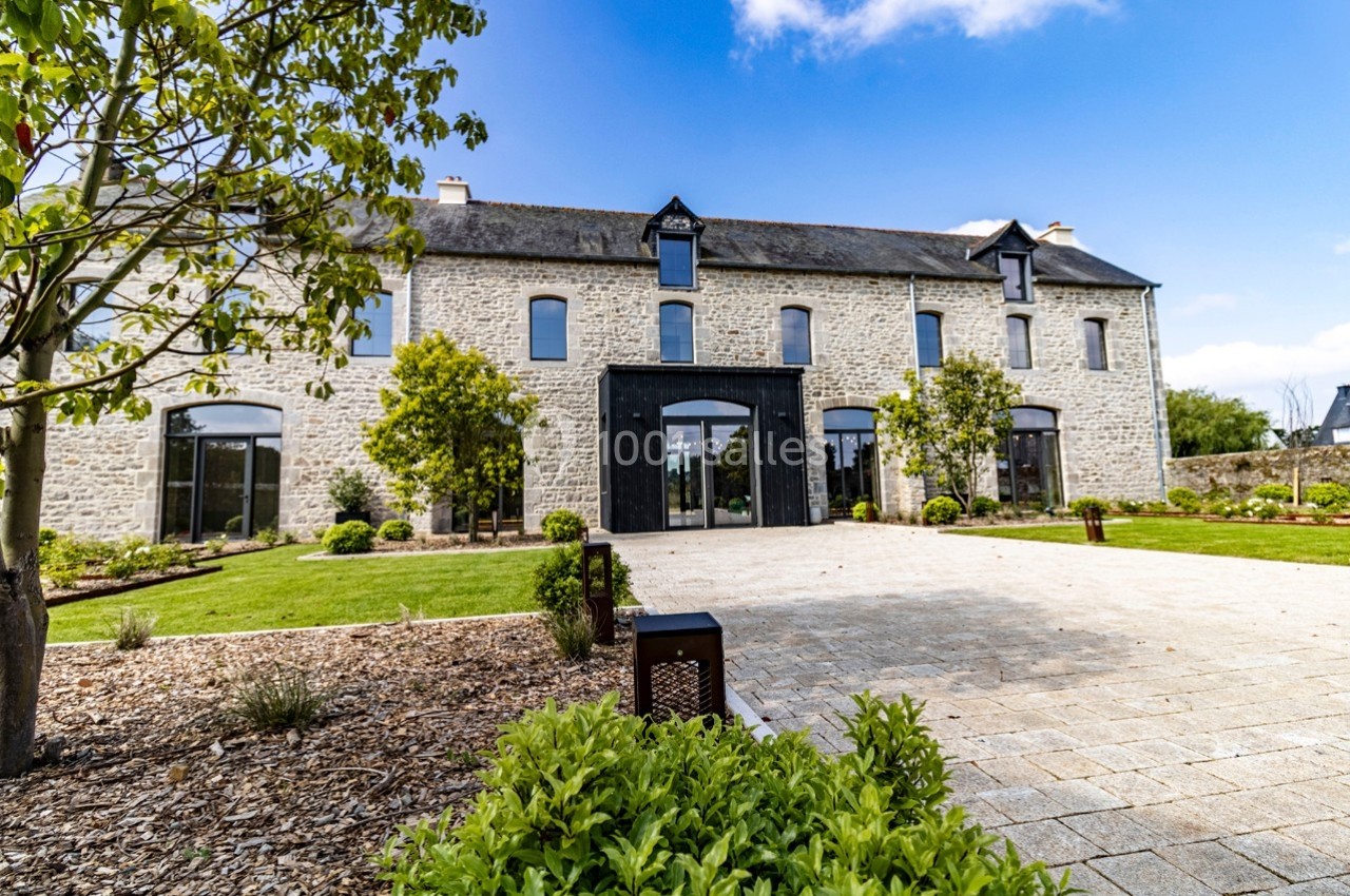 Façade d'une grande maison en pierre rénovée, entourée d'un jardin paysager avec allée pavée.