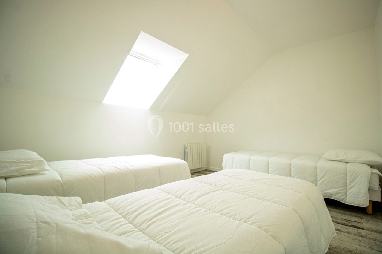 Quatre lits simples alignés dans une chambre lumineuse avec un mur blanc et une fenêtre de toit.