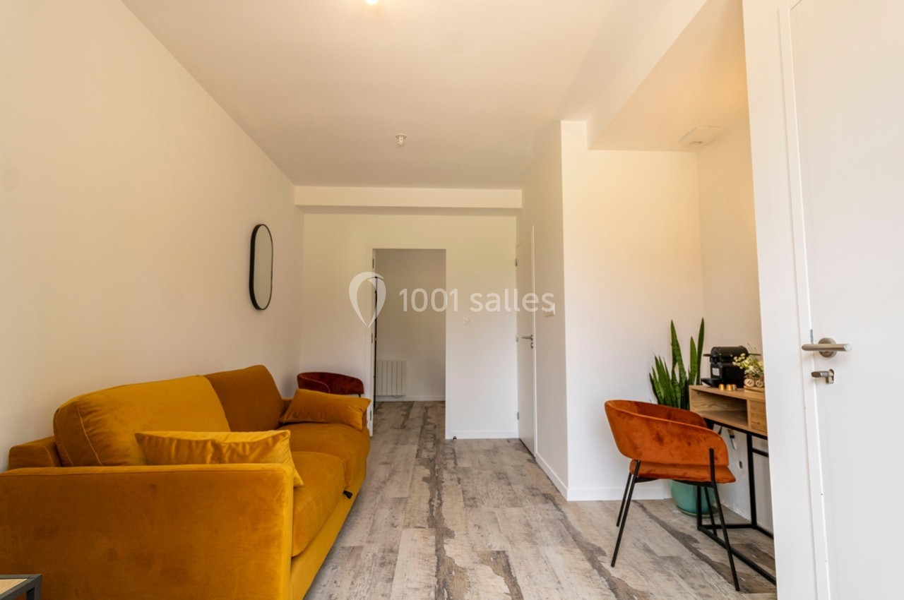 Salon lumineux avec canapé jaune, bureau en bois, chaise orange, plante verte et sol en parquet clair.