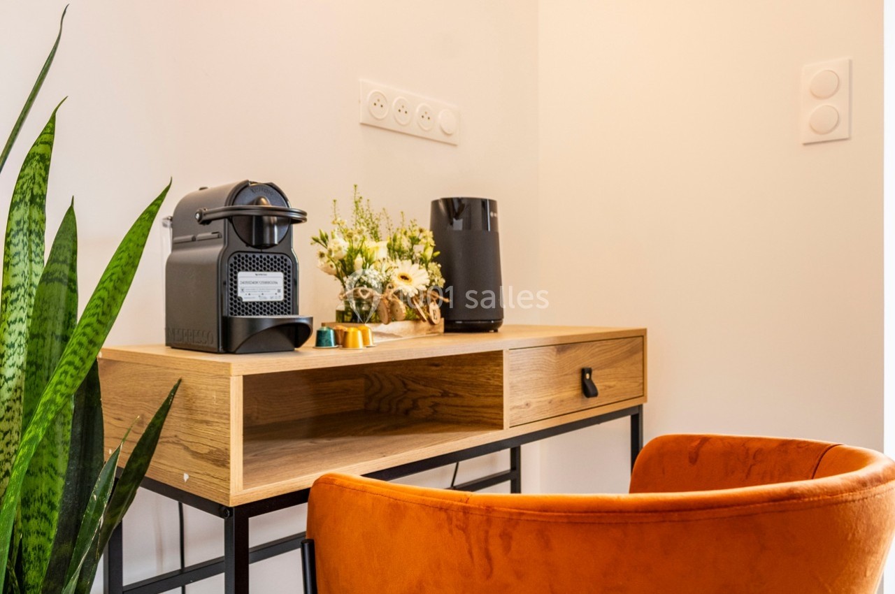 Coin bureau avec une chaise orange, une machine à café, des fleurs et un haut-parleur sur un bureau en bois clair.