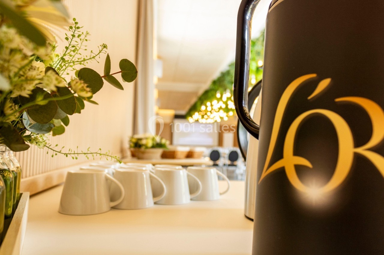 Vue rapprochée d'une cafetière avec le logo ’L'OR’, entourée de tasses blanches et de décorations végétales.