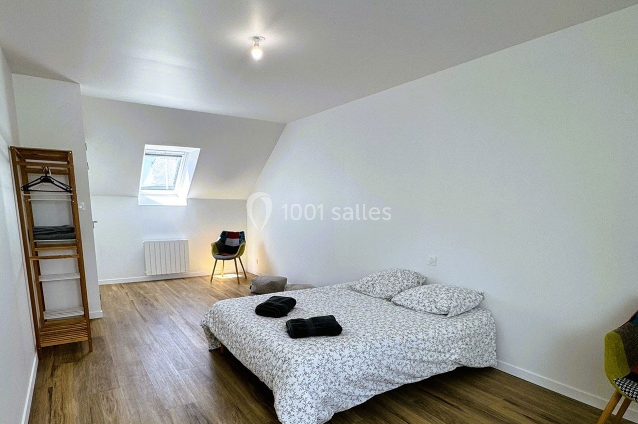 Chambre lumineuse avec lit double, parquet, portant en bois, chaise et fenêtre de toit.