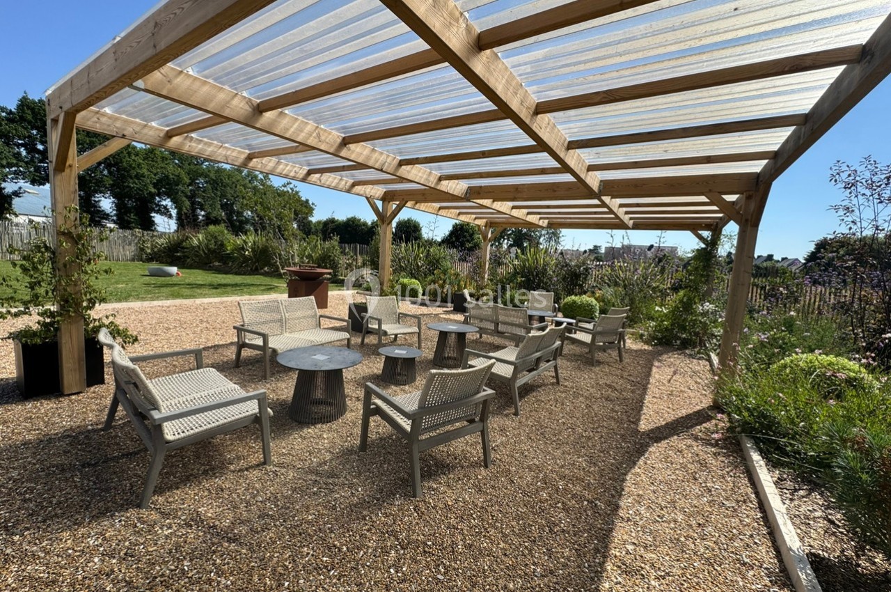 Terrasse extérieure avec pergola en bois, mobilier de jardin en résine et gravier, entourée de végétation.