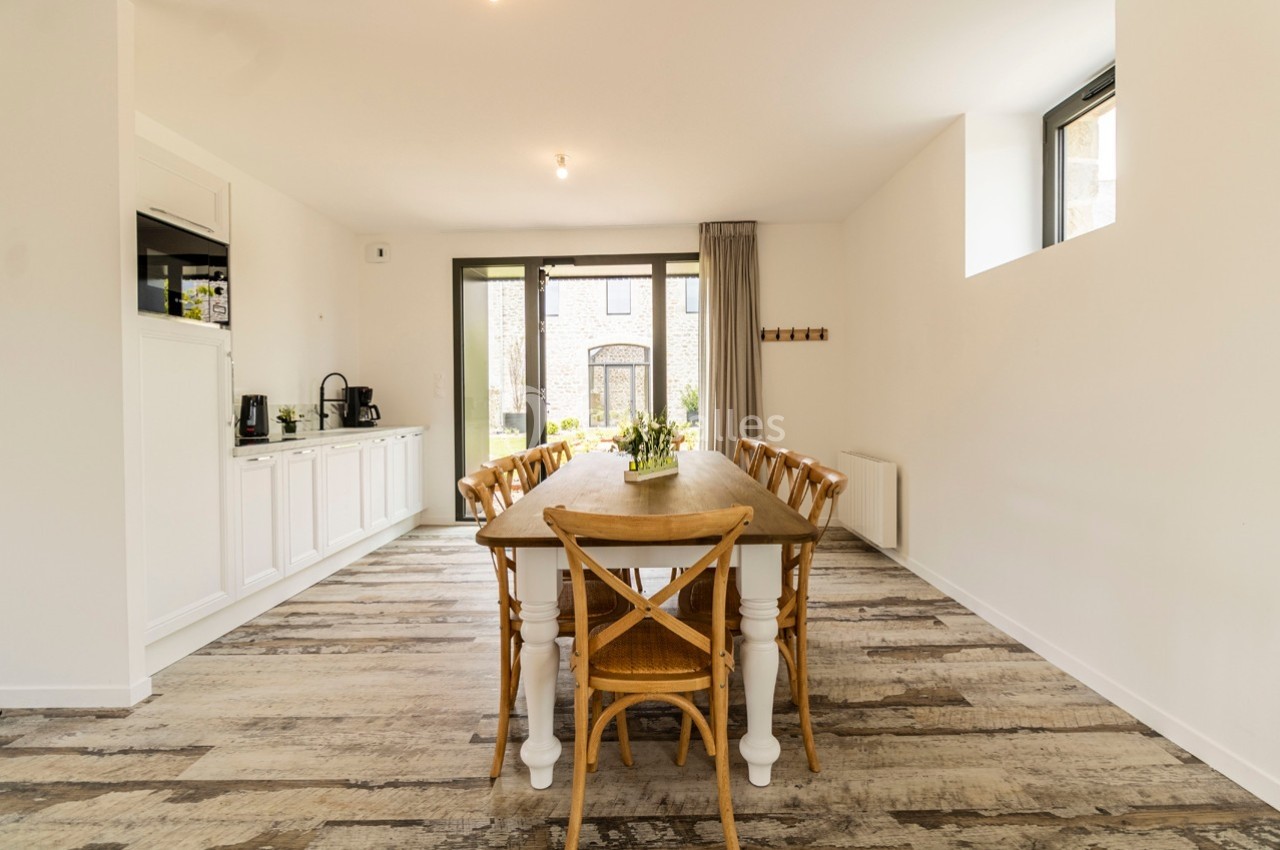 Salle à manger lumineuse avec une grande table en bois entourée de chaises, sol en parquet clair et mobilier blanc.