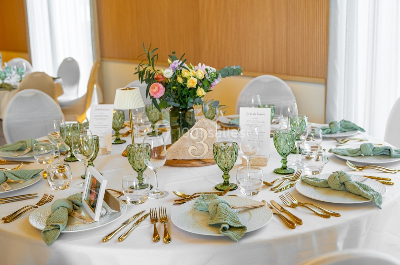 Table élégamment dressée avec vaisselle raffinée, serviettes vertes, verres décoratifs et centre de table floral.