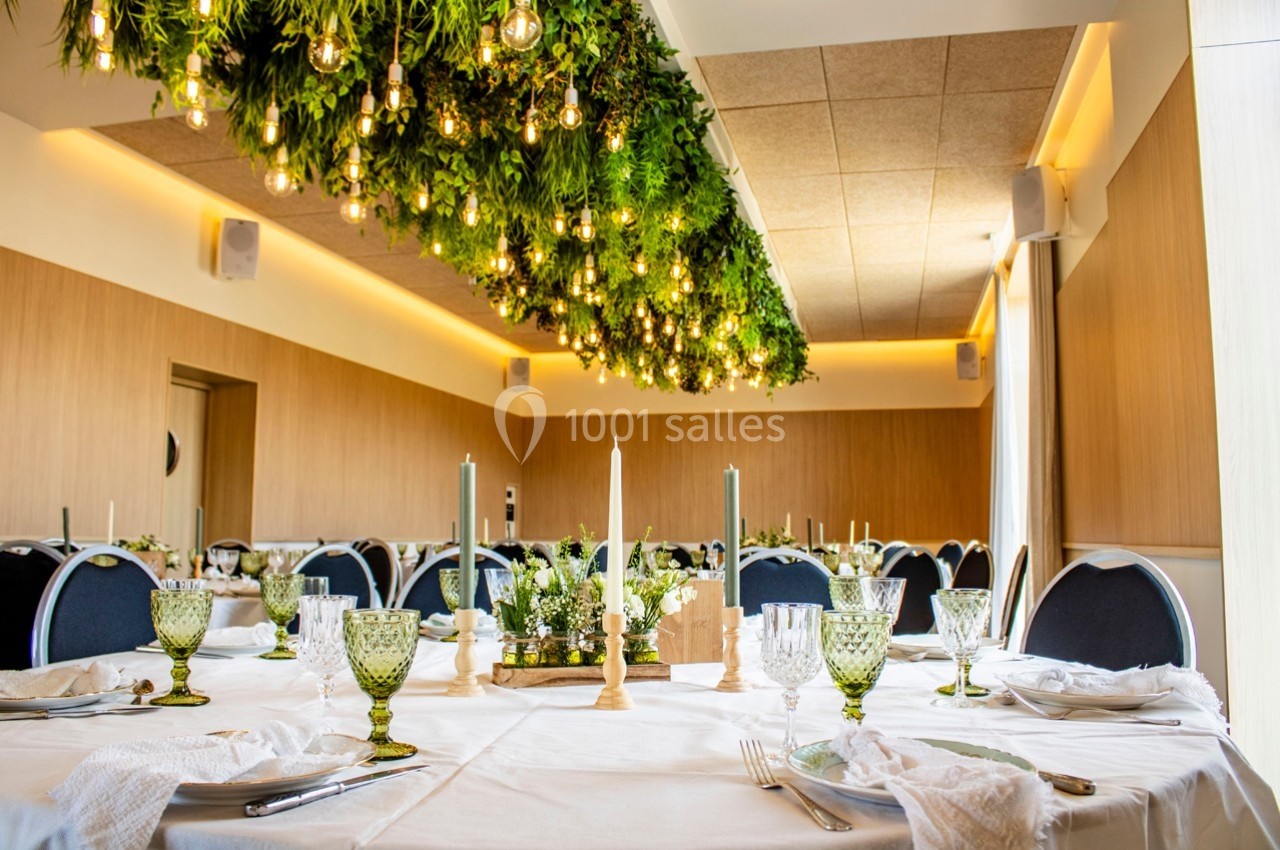 Salle de réception décorée avec des tables dressées, des chandeliers et un plafond orné de plantes et de lumières suspendues.