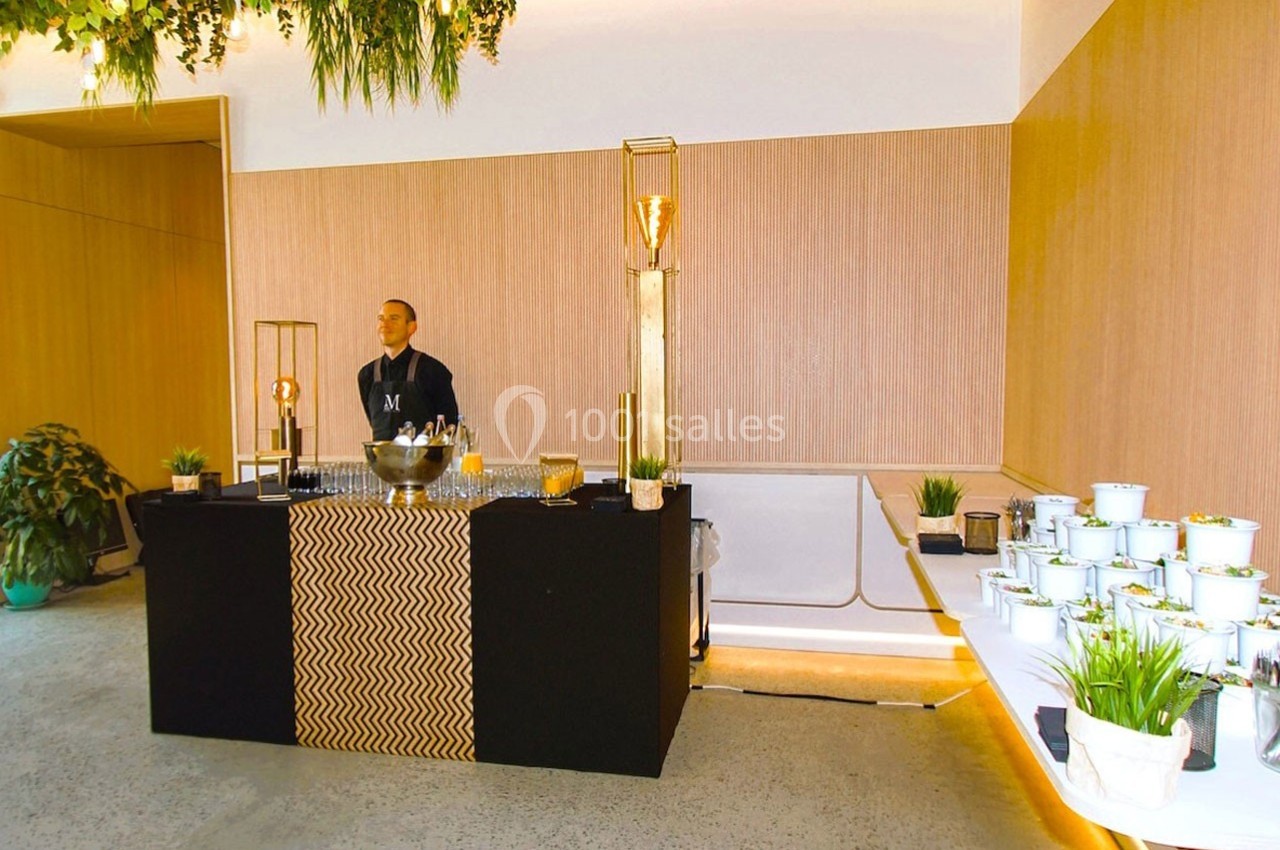 Un buffet élégant avec un serveur derrière un comptoir noir, décoré de plantes et de plats disposés sur une table.