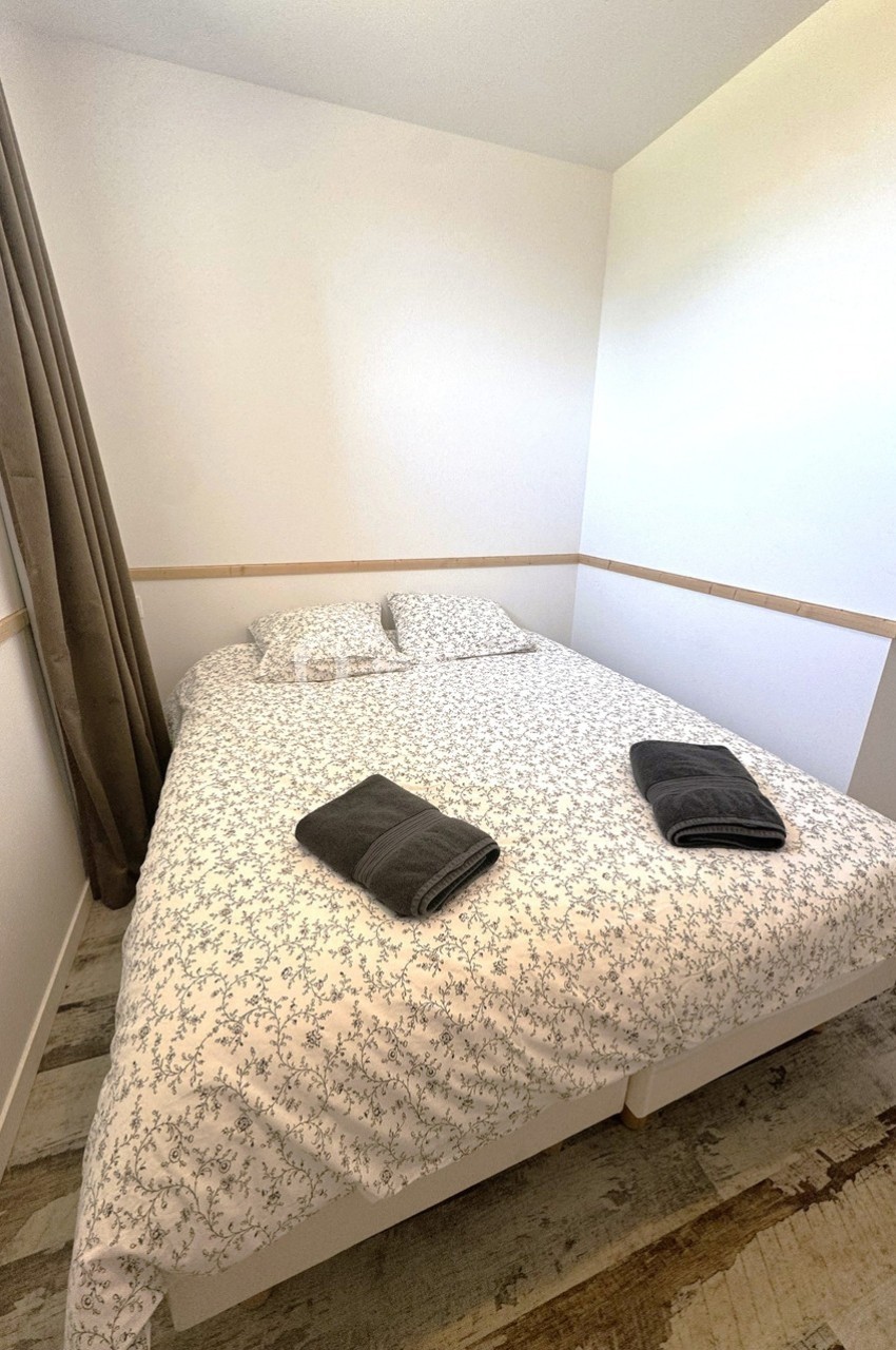 Lit double avec draps à motifs floraux, deux serviettes pliées posées dessus, dans une chambre lumineuse.