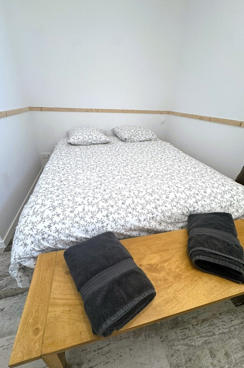 Lit double avec housse de couette à motifs floraux, deux oreillers et serviettes pliées sur un banc en bois.