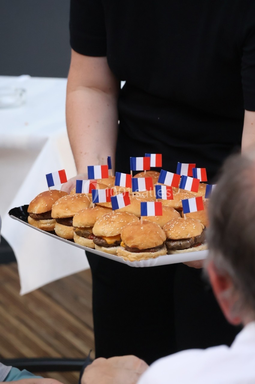 Plateau de mini-burgers décorés de petits drapeaux français, tenu par une personne en tenue noire.