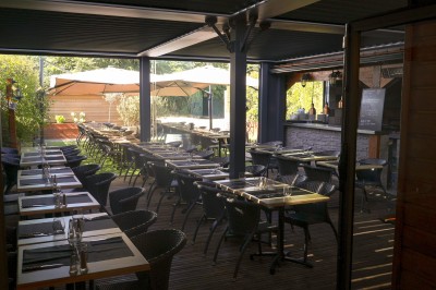 Miniature Location salle Toulouse (Haute-Garonne) - La Cantine d'Horace #3 Terrasse extérieure avec tables et chaises sous des parasols, entourée de verdure et située près d'un bâtiment industriel.