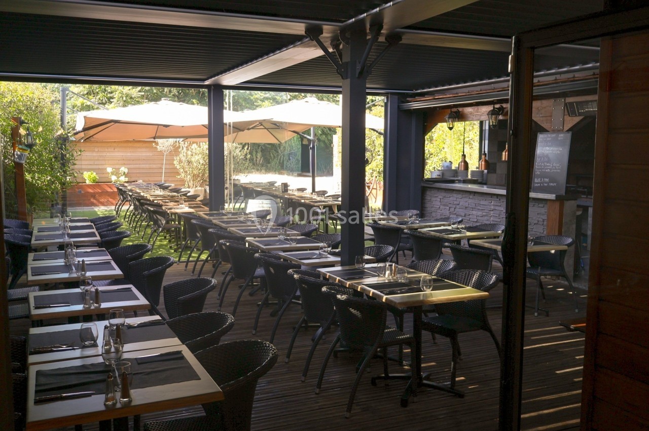 Terrasse couverte d'un restaurant avec des tables dressées, des chaises en osier et des parasols en arrière-plan.