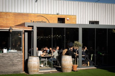 Miniature Location salle Toulouse (Haute-Garonne) - La Cantine d'Horace #7 Terrasse extérieure avec tables et chaises sous des parasols, entourée de verdure et située près d'un bâtiment industriel.