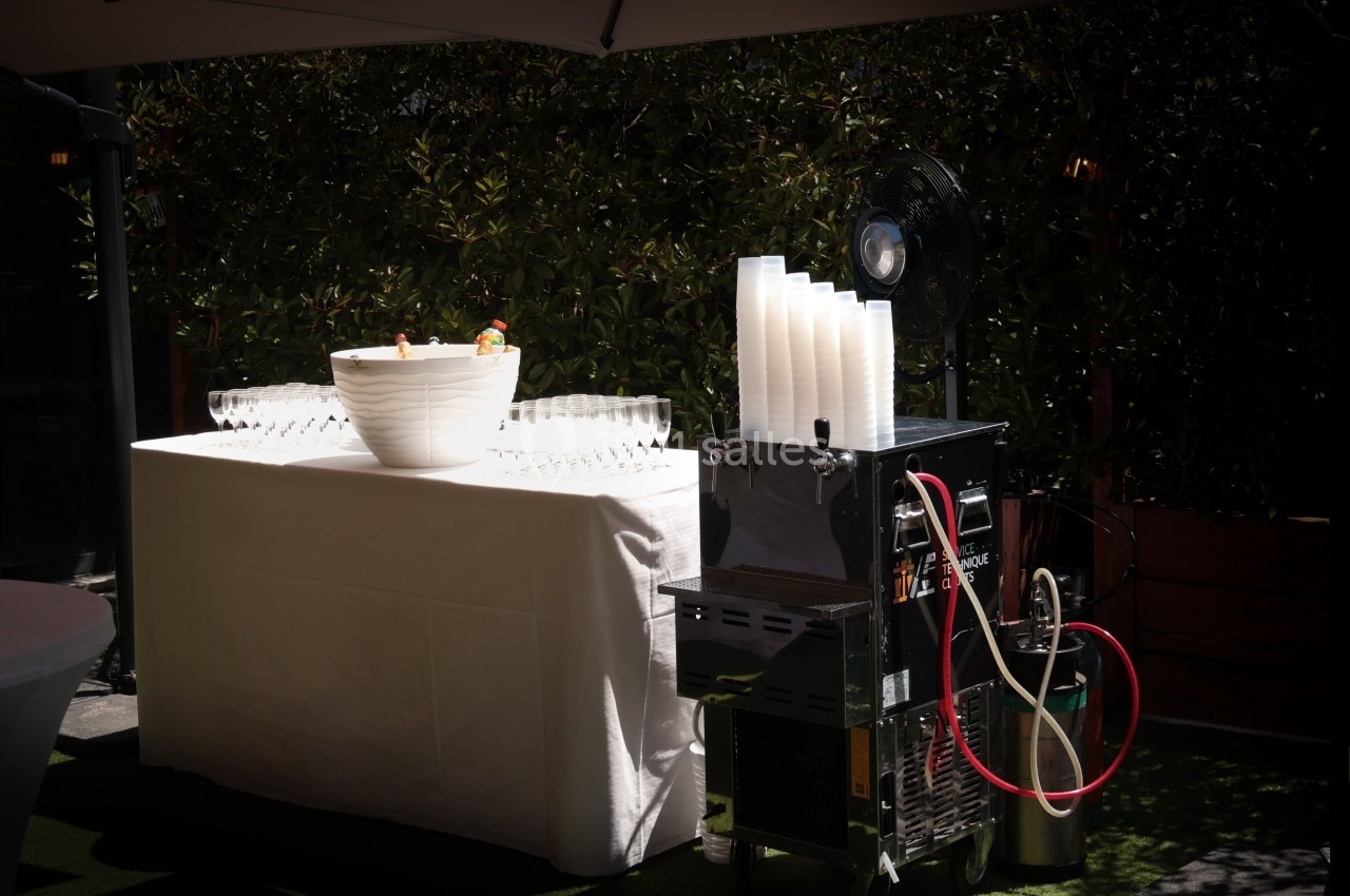 Table dressée avec un saladier de boissons, des verres, et une machine à boissons équipée d'un ventilateur en extérieur.