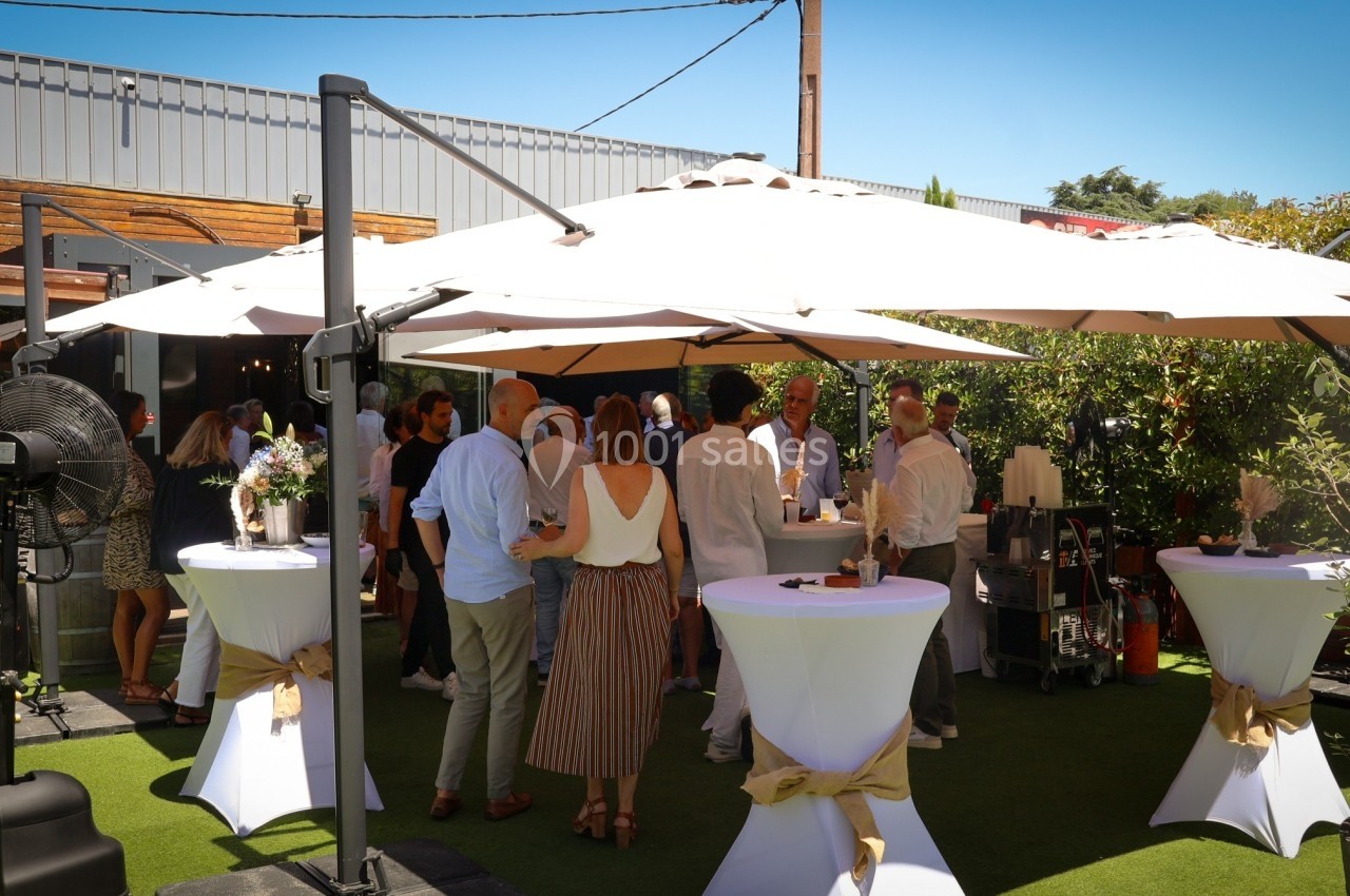 Groupe de personnes discutant sous des parasols lors d'un événement en extérieur, avec tables hautes décorées.