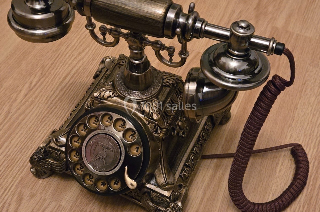Téléphone ancien en métal avec cadran rotatif, posé sur un sol en bois clair.