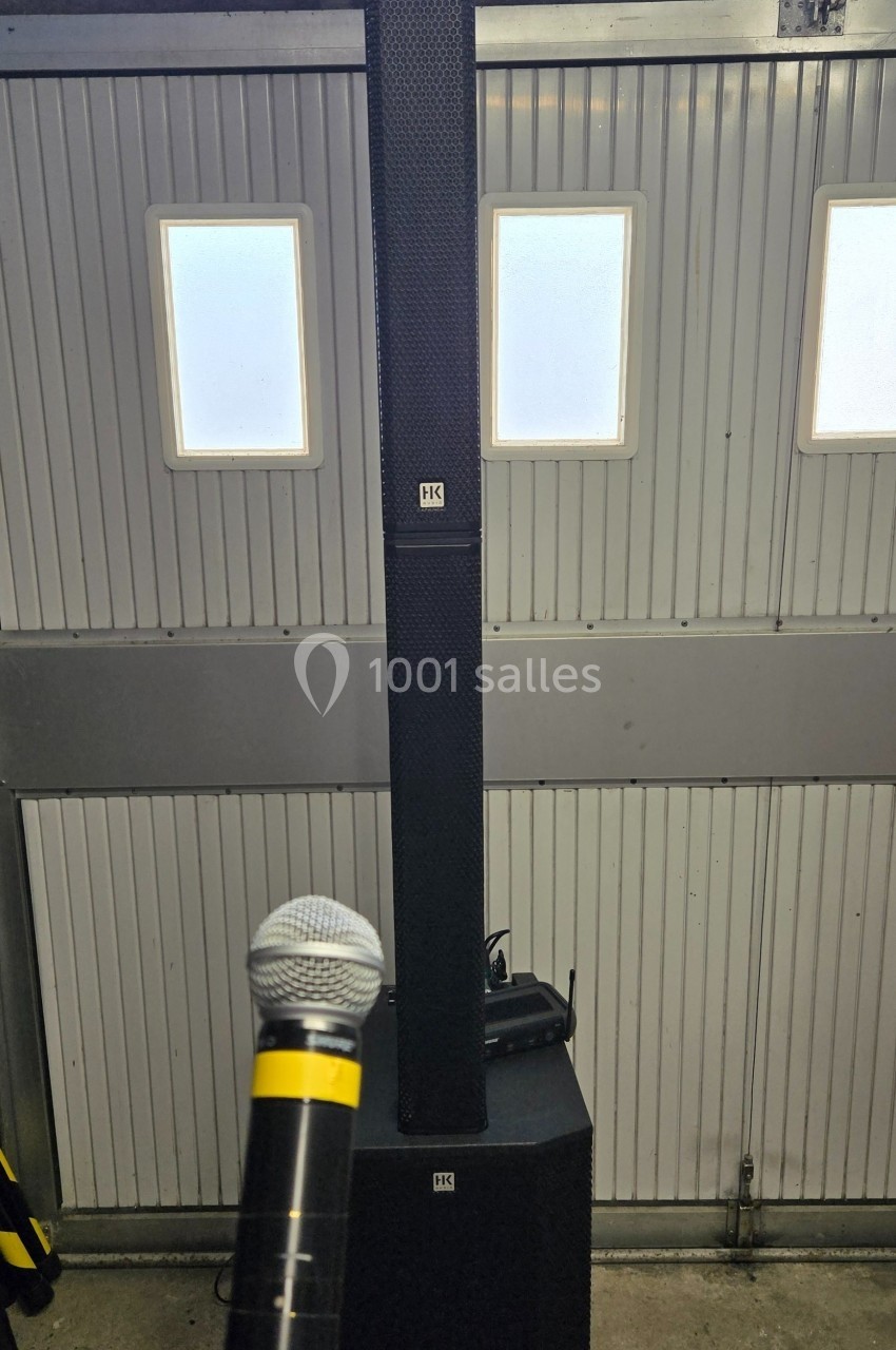 Système de sonorisation avec une colonne d'enceintes et un microphone tenu devant, dans un garage lumineux.