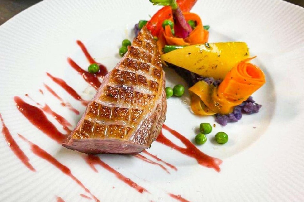 Assiette gastronomique avec magret de canard, purée violette, légumes colorés et sauce rouge en décoration.