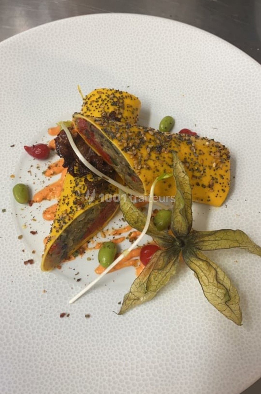 Assiette gastronomique avec rouleaux garnis, graines, sauce colorée, physalis et légumes décoratifs.