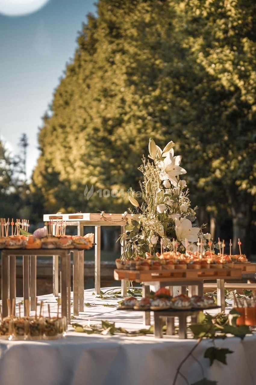 Buffet en extérieur avec des amuse-bouches sur des présentoirs et une décoration florale, entouré d'arbres.