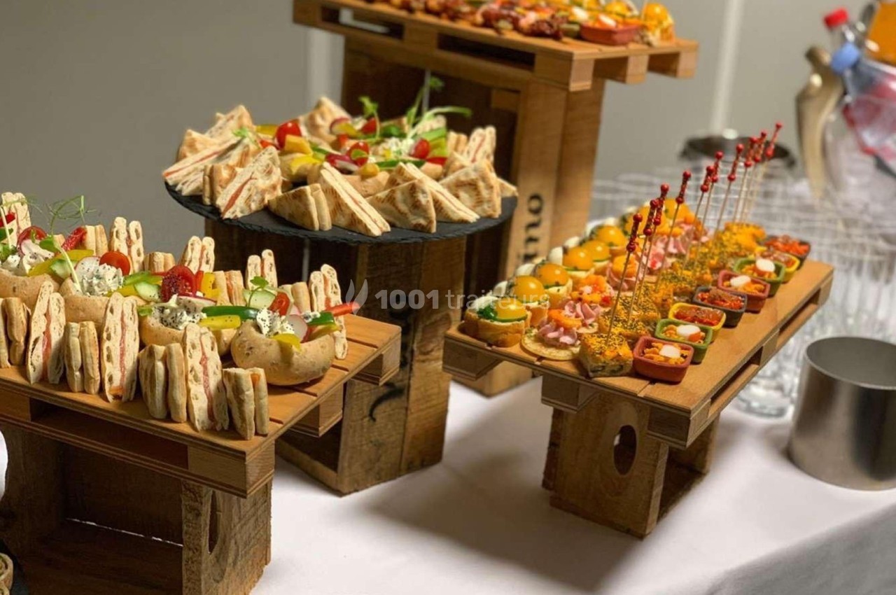 Plateau de buffet avec assortiments de sandwichs, brochettes, verrines et amuse-bouches variés sur des présentoirs en bois.