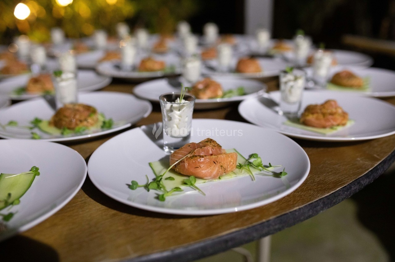 Assiettes dressées avec du saumon fumé, des pousses vertes et des verrines de sauce blanche sur une table en bois.