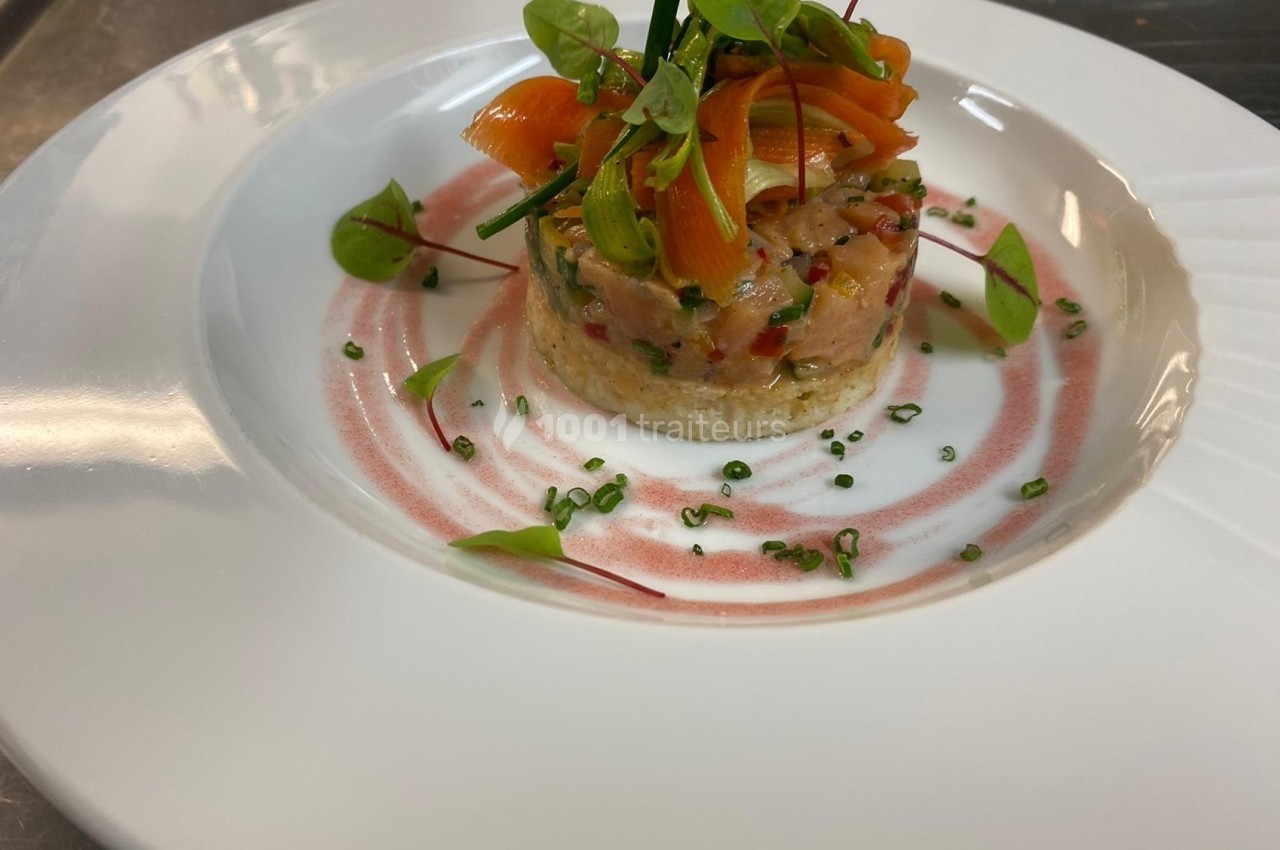Tartare de saumon dressé sur une assiette blanche, décoré de fines herbes et d'une sauce rose en spirale.