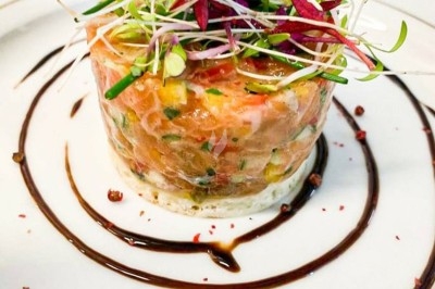 Tartare de saumon garni de jeunes pousses et entouré de filet de sauce balsamique sur une assiette blanche.