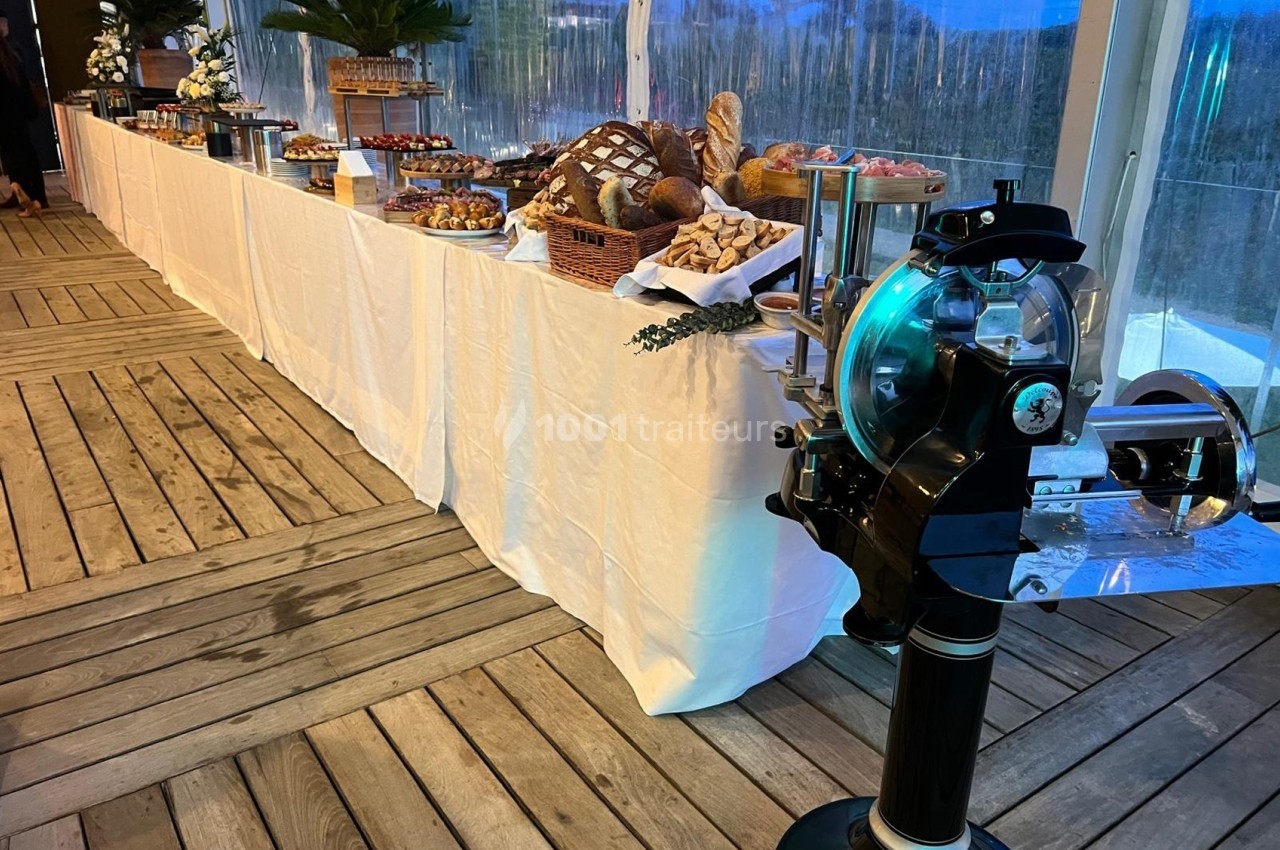Table de buffet garnie de pains, viennoiseries et pâtisseries, avec une trancheuse en premier plan.