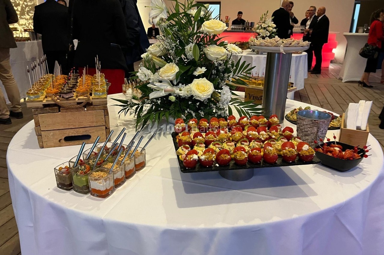Table ronde dressée avec des verrines, des amuse-bouches et une décoration florale, lors d'un événement en intérieur.