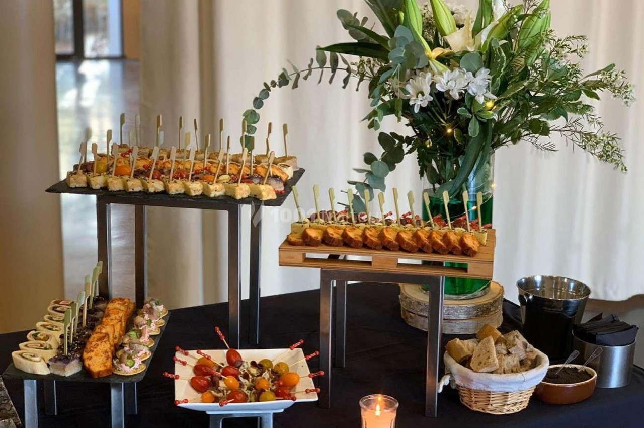 Buffet avec brochettes, amuse-bouches variés et fleurs en arrière-plan sur une table noire.