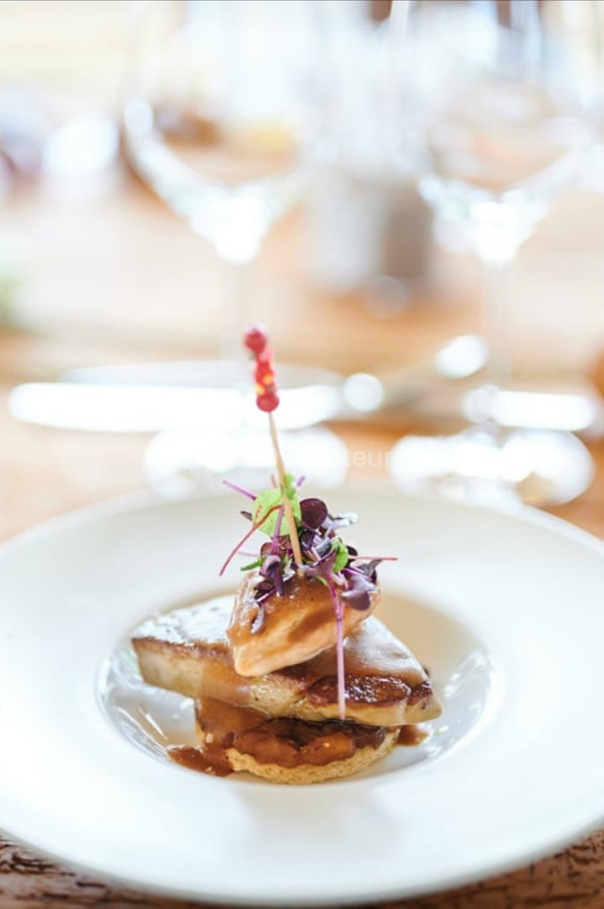 Assiette gastronomique avec foie gras, garniture de pousses et sauce, présentée sur une table élégamment dressée.